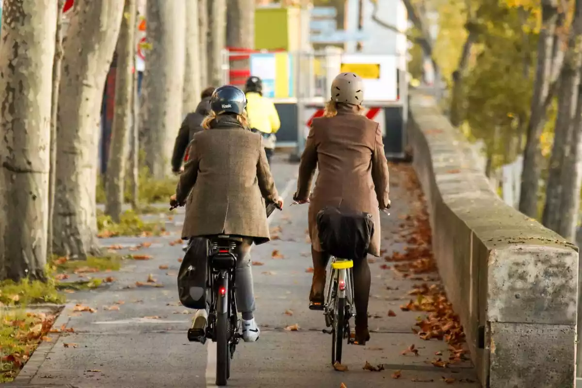 Carril bici de una ciudad con dos mujeres de espaldas circulando con sus bicicletas en otoño