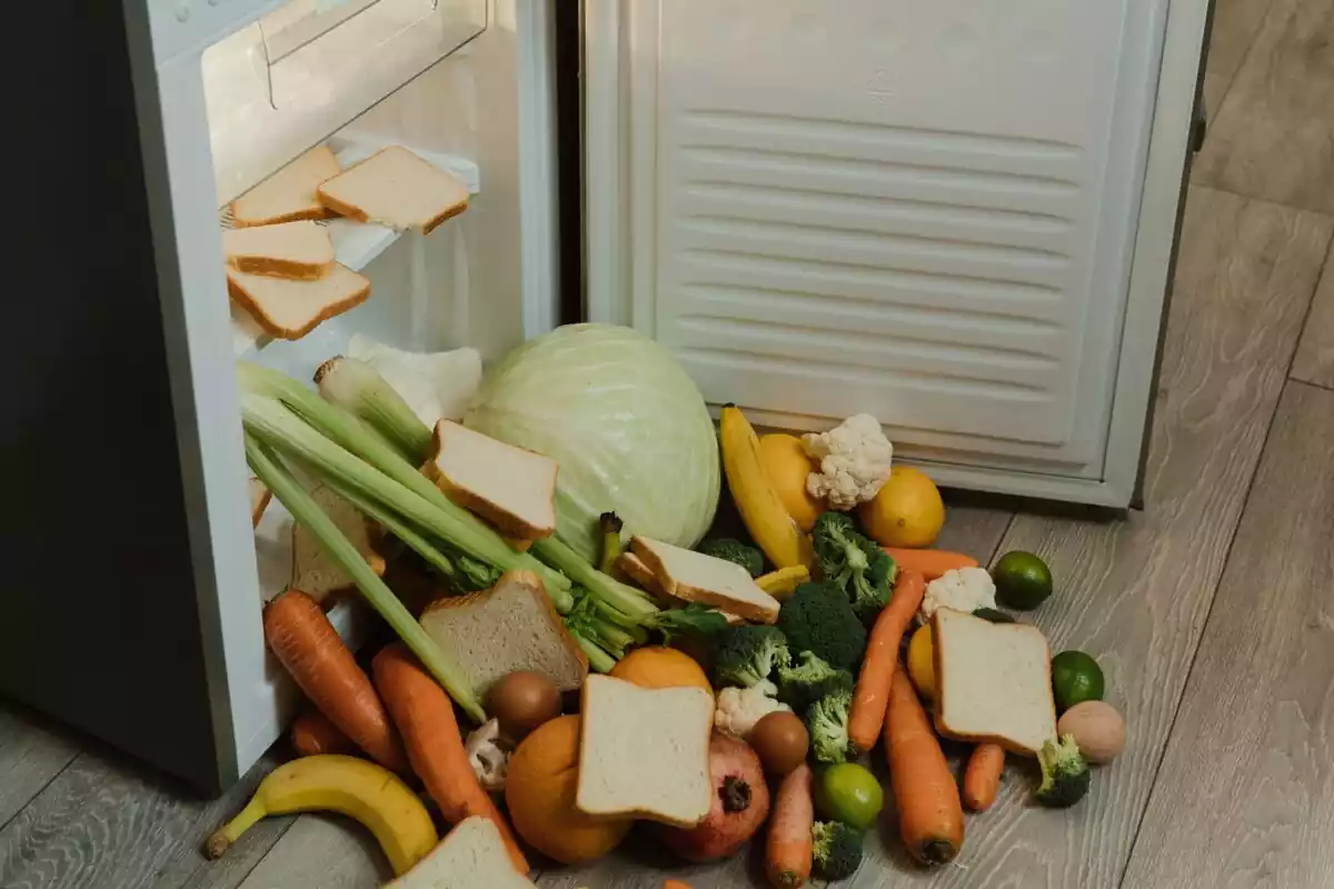 Imagen de un frigorífico abierto con comida tirada por el suelo