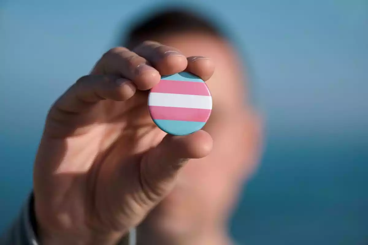 Mano sujetando una chapa con la bandera transexual