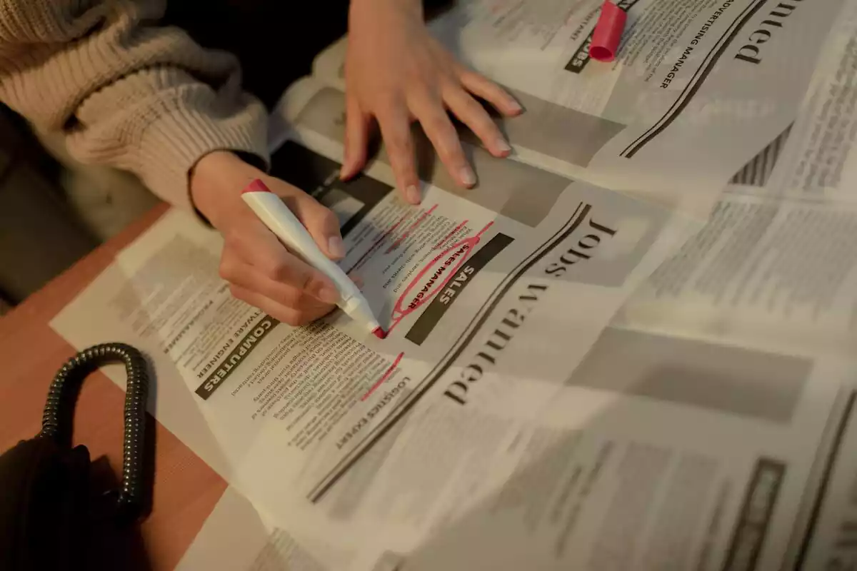 Mujer buscando empleo a través de un diario seleccionando con un rotulador rojo la mejor opción