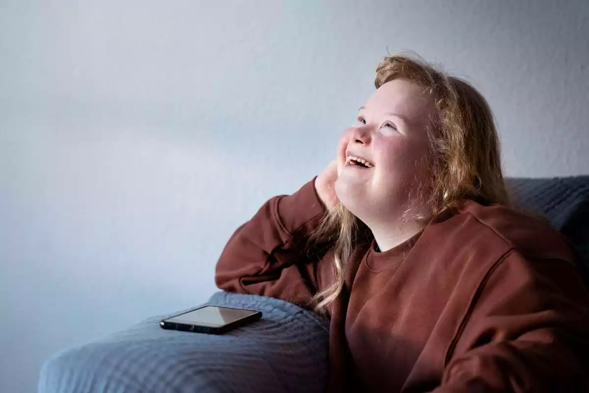 Niña con síndrome de Down sonriendo mirando arriba sentada en un sofá