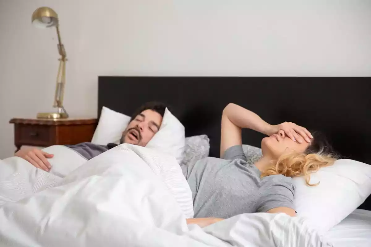 Un hombre roncando en su cama junto a su mujer despierta por los ronquidos