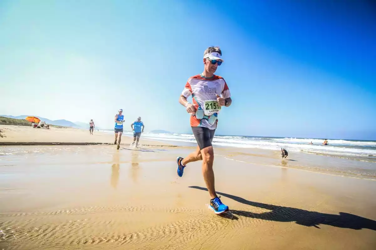 Hombre corriendo por una playa junto a otros atletas en un maratón