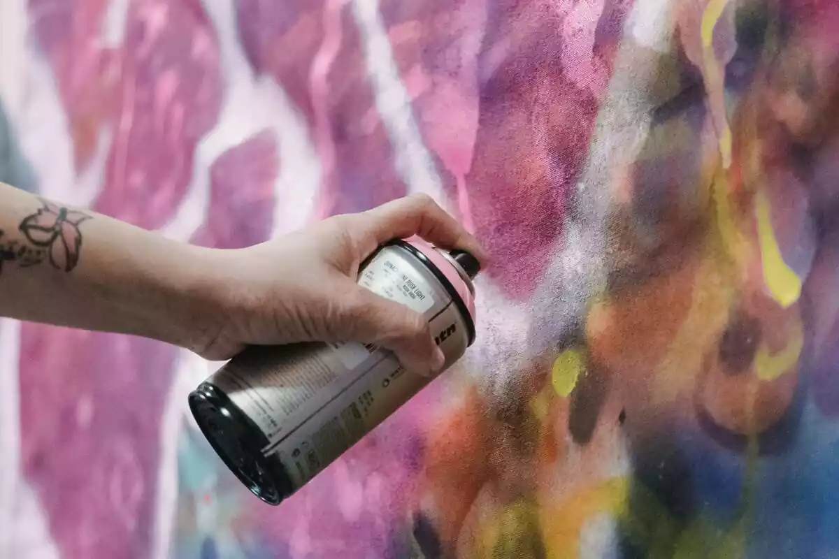 Mujer con un spray de grafiti en una pared dibujando en tonos rosas