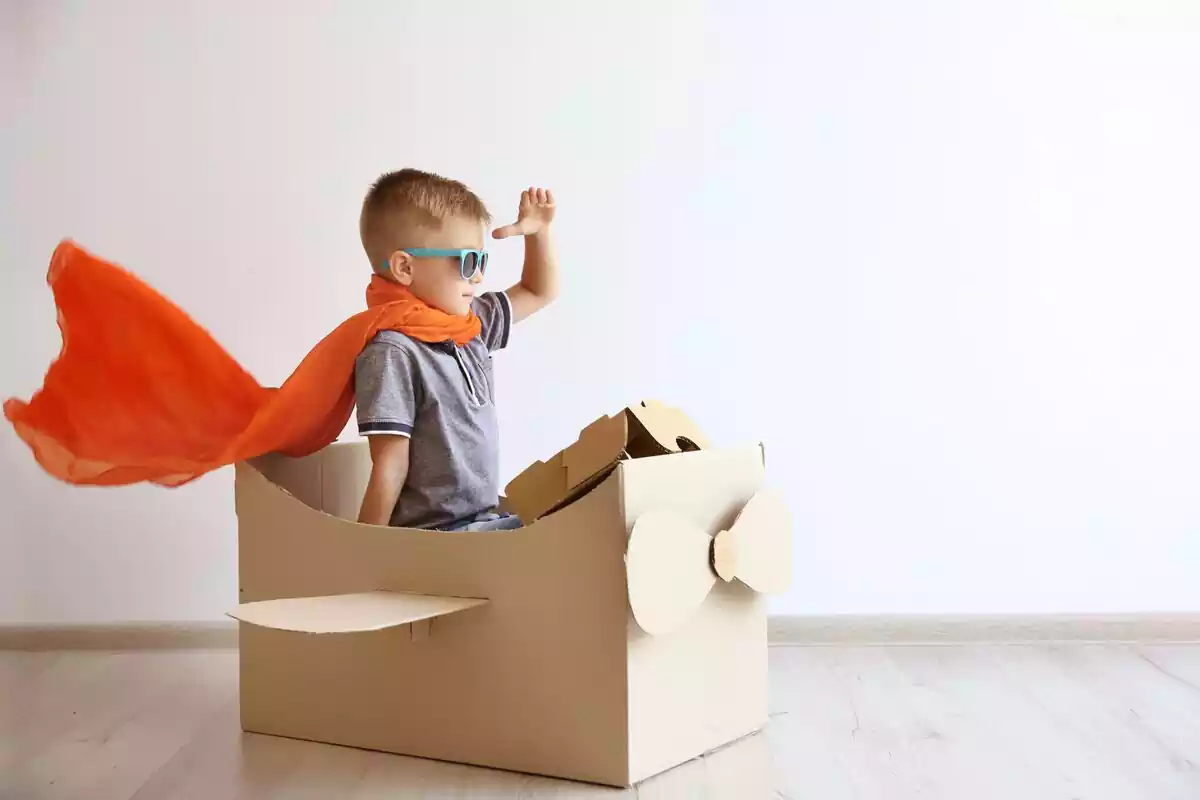 Un niño dentro de una caja de cartón simulando ser un avión con una capa