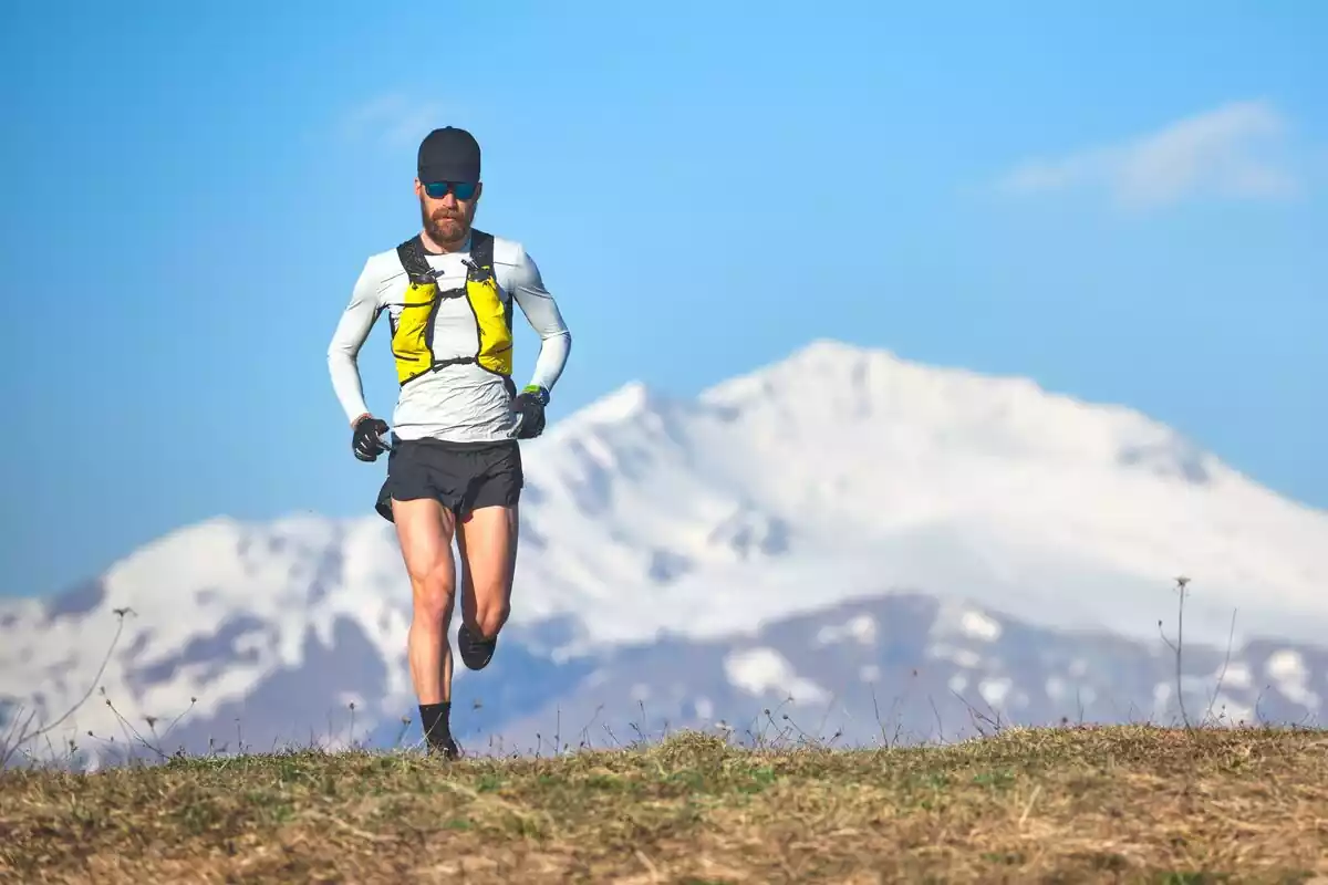 Hombre corriendo en el monte con una montaña nevada de fondo